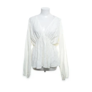 Krämvit spetsblus från Vila - Säljer en romantisk krämvit blus från Vila med v-ringad hals och långa ärmar. Blusen är tillverkad i spets med ett skirt, broderat mönster och har en lätt volang vid midjan. Perfekt för dig som gillar en feminin och luftig stil.