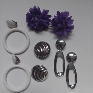 Klipps örhängen - 80-tal örhängen. 1. Vita runda i plast. 2. Silverfärgad metall med vågor mönster. 3. Silverfärgade plast ĥängande. 4 lila tyg blommor