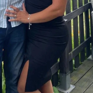 Svart tight klänning med slits - Snygg svart klänning med v-ringning, korta ärmar och en hög slits på sidan. Klänningen har en tight passform som framhäver figuren och är perfekt för dig som vill sticka ut. Materialet känns mjukt och följsamt mot kroppen. Väldigt strechig