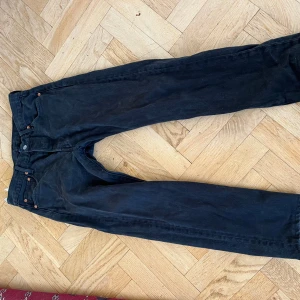 Svarta Levi's 501 jeans W30 L30 - Svarta Levi's 501 jeans med klassisk rak passform och knäppning fram. Jeansen har fransade benslut för en cool, avslappnad vibe. Tillverkade i slitstarkt denim med fem fickor och ikoniska nitar. Perfekta för dig som gillar tidlös streetstil. Upsydda en cm eller två