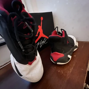 Nike Air Jordan sneakers svart/röd/vit - Säljer ett par feta Nike Air Jordan sneakers i svart, rött och vitt. Skorna har klassisk Jordan-design med snörning, rund tå och coola detaljer. Insidan är röd och ovandelen är i skinn och syntet. Perfekta för dig som vill sticka ut med en ikonisk streetstil.