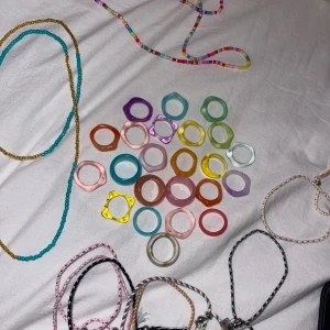 Färgglada ringar och pärlhalsband - Säljer ett gäng coola ringar i olika färger och former, gjorda av plast och resin. Färgerna är bland annat lila, rosa, blå, grön, gul, orange och transparent. Medföljer även pärlhalsband i turkos, guld och regnbågsfärger samt flätade armband i olika mönster.
