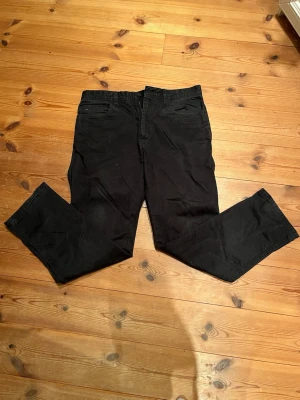 Svarta slim fit byxor från J.Lindeberg - Snygga svarta byxor från J.Lindeberg i slim fit-modell. Byxorna har klassisk femficksdesign, diskret logga vid fickan och är tillverkade i ett mjukt bomullsmaterial med lite stretch. Perfekta för en clean och stilren look.