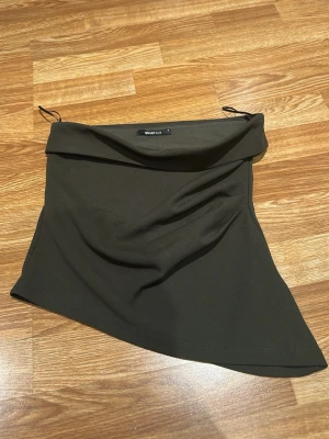 Grön axelbandslös tubtopp Ginatricot - Trendig grön axelbandslös tubtopp från Ginatricot med asymmetrisk nederkant. Toppen har en enkel och stilren design, perfekt att matcha med jeans eller kjol. Mjuk och stretchig för en bekväm passform.