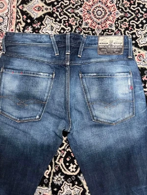 Replay anbass FCB jeans blå, rak modell - Snygga blå jeans från Replay i samarbete med FC Barcelona. Klassisk femficksmodell med raka ben och diskreta slitningar. Jeansen har Replay-logga på fickan och FC Barcelona-detaljer i midjan. Perfekta för dig som gillar grish stil