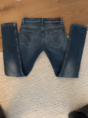 Dondup George - Säljer ett par blå slim fit jeans från dondup med klassisk femficksmodell och snygga slitningar på låren. Jeansen har en något tvättad look och kontrastsömmar på bakfickorna. Perfekta för en avslappnad och trendig stil.