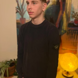 Svart stickad tröja från Stone Island - Snygg svart stickad tröja från Stone Island med klassisk rund halsringning och ikonisk logotyp-patch på vänster ärm. Tröjan har ribbade muddar vid ärmslut och nederkant. Perfekt för dig som gillar stilrena och exklusiva plagg.