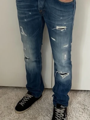 Blå slitna jeans med raka ben - Säljer ett par blå jeans med raka ben och flera slitningar framtill. Riktigt snygga och i bra skick.