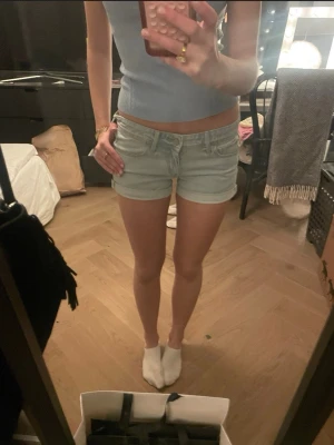 Ljusblå denimshorts med upprullad kant - Säljer ett par ljusblå denimshorts med upprullad kant och klassisk femficksdesign. Shortsen har normal passform och midja, perfekta för varma dagar. Inga synliga loggor eller märken. Snygga att matcha med crop tops eller t-shirts!