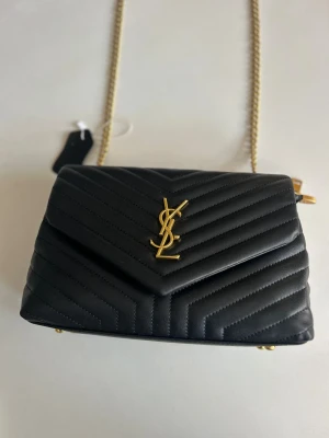 Svart axelremsväska handväska guld kedja skinn läder imitation - Snygg axelremsväska med logga, helt ny och oanvänd. Guldig kedja.