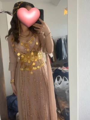 Traditionell beige kaftan med guldmynt - Säljer min jätte fina kurdiska klänning ( lawandi ) som är skräddarsydd i Irak. Klänningen e en blandning mellan baby rosa och beige färg. Den är super fin med massa kristaller på den. Klänningen är bara använd i några timmar. Pris går att diskuteras vid snabb affär.