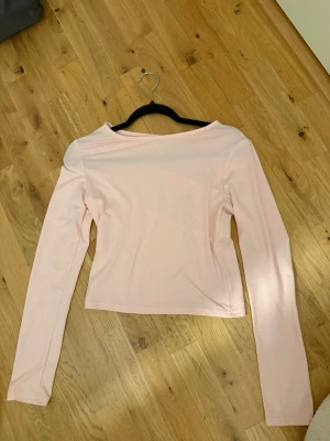 Ljusrosa långärmad topp - En stilren ljusrosa långärmad topp med rak passform och enkel design. Toppen har en något bredare halsringning och är tillverkad i ett mjukt, stretchigt material som känns bekvämt mot huden. Perfekt att matcha med jeans eller kjol.