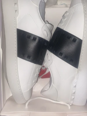 Valentino Garavani Open sneakers vit/svart - Säljer ett par helt nya Valentino Garavani Open sneakers i vitt skinn med bred svart rem och nitar på sidorna. Skorna kommer med dust bag och allt annat!