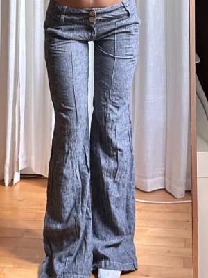 Grå kostymbyxor med utsvängda ben - Säljer ett par grå kostymbyxor med låg midja och utsvängda ben. Byxorna har framfickor, knappgylf och markerade sömmar längs benen för en snygg retrovibe. Perfekta för dig som gillar en avslappnad men trendig stil. Lånade bilder från hon jag köpte utan men aldrig använda 