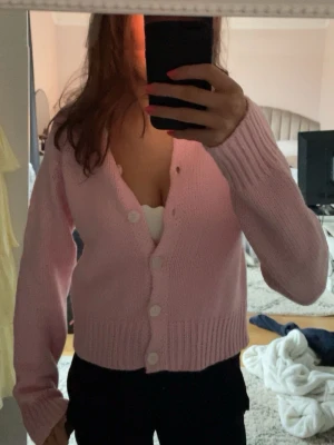 Ljusrosa stickad kofta med knappar - Säljer en söt ljusrosa stickad kofta med stora vita knappar och ribbade muddar. Koftan har en croppad passform och långa ärmar, perfekt att slänga över en topp. Enkel och stilren design som passar till mycket. Använt cirka 2 gånger synd inget.