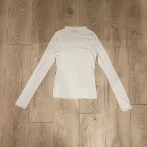 Vit långärmad polotopp - Klassisk vit långärmad polotopp i mjukt tunnt material med ett sött stickat hålmönster. 