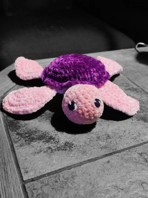 Mysig sköldpadda, handgjord - Supergullig virkad sköldpadda i mjuk plysch med lila skal och rosa ben, huvud och svans. Perfekt som present eller mysig inredningsdetalj. Sköldpaddan har stora broderade ögon och är tillverkad i ett fluffigt material som är skönt att krama. Prefekt som present till äldre och små. 