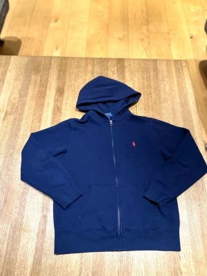 Polo Ralph Lauren Zip Hoodie – Marinblå – Mycket fint skick - Säljer en snygg och klassisk zip-hoodie från Polo Ralph Lauren i marinblå färg med röd logga. Väldigt stilren och lätt att matcha.  ✔️ Mycket fint skick ✔️ Dragkedja och passform är som de ska ✔️ Äkta Polo Ralph Lauren ✔️ Skön och bra kvalitet  Perfekt till vardag, skola eller chill outfits.  Kan skickas eller mötas upp (köparen står för frakt om den skickas).