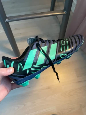 Adidas Messi fotbollsskor svart/grön - Säljer ett par Adidas Messi fotbollsskor i svart med gröna detaljer och mönster. Storlek 36 1/3. Skorna har klassiska tre ränder på sidan, snörning och låg profil. Yttermaterialet är syntet och sulan har dobbar för spel på gräs. Bra skick. Bra för dig som vill dribbla som Messi på planen