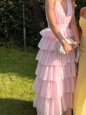 Balklänning, ljusrosa med volanger - En lång ljusrosa klänning med flera lager volanger och  v-ringning. Klänningen har breda axelband och markerad midja. Den är från Bubbelroom 💕Jag är 172cm och hade klackar på mig på bilderna så den funkar även för längre personer. Endast använd en gång!