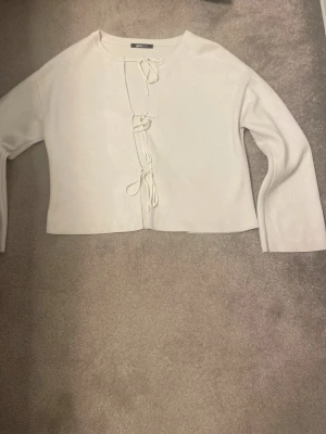 Vit kofta med knyt framtill - Trendig vit, finstickad kofta med tre knytband framtill och lång ärm. Rak passform och mjukt material som känns skönt mot huden. Storlek s, stämmer bra i storlek. Är från Gina tricot 