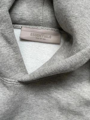 Grå hoodie Essentials  - Grå Essentials hoodie. Den är större i storleken, jag brukar ha S och denna var för stor 