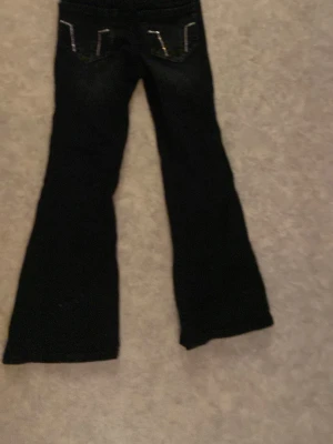 Svarta bootcut jeans med fickdetaljer - Snygga svarta bootcut jeans med dekorativa sömmar på bakfickorna. Jeansen har utsvängda ben och klassisk femficksdesign. Perfekta för dig som gillar en retrostil och vill ha ett par jeans som sticker ut lite extra.