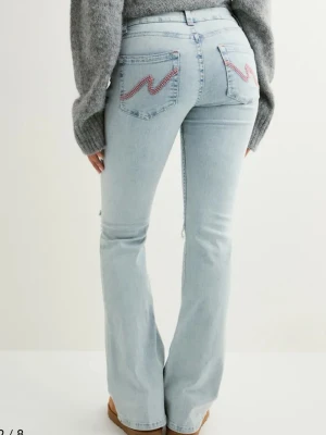 Ljusblå bootcut jeans med slitningar - Säljer ett par ljusblå bootcut jeans med slitna knän och broderade detaljer på bakfickorna. Jeansen har klassisk femficksdesign och är i mjukt denimtyg. Perfekta för en avslappnad och trendig look.