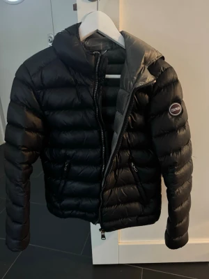 Svart dunjacka från Colmar - Snygg svart dunjacka från Colmar med quiltad design och två dragkedjeförsedda fickor. Jackan har hög krage, Colmar-logga på ärmen och grått innerfoder. Perfekt för kalla vinterdagar och riktigt stilren look. Storlek 42 IT och passar bra på mig som bär xs/s💕