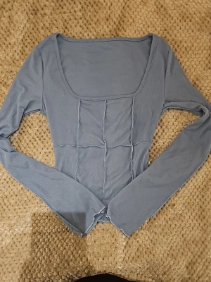 Blå ribbad topp från Dazy - Snygg blå långärmad topp från Dazy med ribbad struktur och fyrkantig ringning. Tillverkad i mjuk och stretchig polyesterblandning som sitter bekvämt. Perfekt att styla med jeans eller kjol för en trendig look.