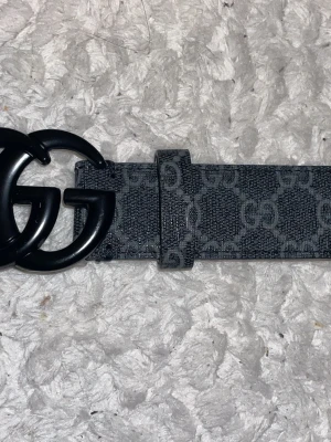 Svart GG-bälte från Gucci - Svart gucci bälte med grå gg mönster, använt fåtal gånger.