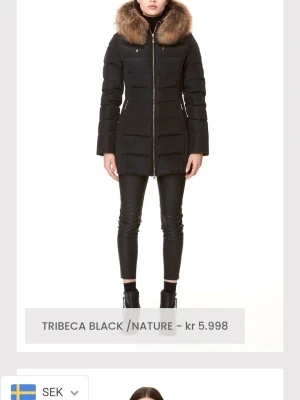 Svart dunjacka med pälskrage - Snygg svart dunjacka från Mackage med figurnära passform och stor, lyxig pälskantad huva. Jackan har guldfärgad dragkedja framtill och quiltad design som ger en modern look. Perfekt för kalla vinterdagar.