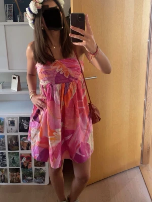 Färgglad kort sommarklänning med axelband - Supersöt rosa-orange kortklänning med tunna axelband. Klänningen har en luftig passform och rynkade detaljer upptill. 