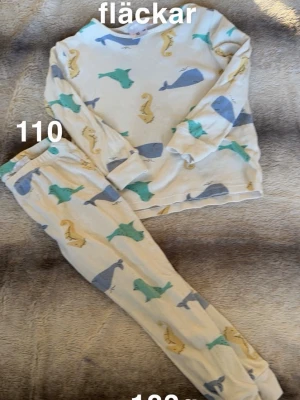 Vit pyjamas med havsdjur - Mysig vit pyjamas med långärmad tröja och byxor, täckt av färgglada havsdjur som valar, sjöhästar och sälar i blått, grönt och gult. Perfekt för dig som gillar lekfulla mönster. 🌸 Fläckar. Storlek 110
