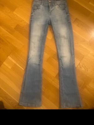 Ljusblå bootcut jeans med mid midja - Säljer ett par ljusblå bootcut jeans med mid midja och klassisk femficksdesign. Jeansen har snygg slitning framtill och lätt utsvängda ben. Tillverkade i mjukt denimtyg som sitter skönt och ger en avslappnad look.