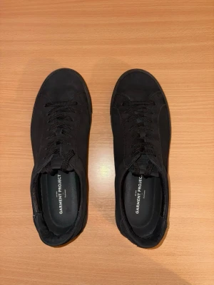 Garment Project Sneakers (nubuck-läder) - Ett par svarta skor från Garment Project i nubuck-läder, storlek 40.  Skorna är väldigt varsamt använda och i princip nyskick. Enda anmärkningen är ett litet snitt vid hälen (vänster sko), syns knappt i verkligheten (se bild).  Butikspris 1800kr  Material: • Överdel: 100% nubuck • Foder/övre foder: 100 % läder • Innersula: polyuretan-skum • Yttersula: gummi