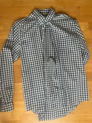 Rutig skjorta från Peak performance stlL - Säljer en klassisk rutig skjorta från Peak Performance i storlek L. Skjortan har svart, vit och grå färgton, lång ärm och knappar framtill. Tillverkad i mjuk bomull, perfekt för en avslappnad men ändå stilren look.
