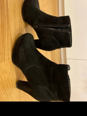 Svarta mocka boots med klack - Säljer ett par svarta boots i mocka med rund tå och hög klack. Skorna har dragkedja på sidan för enkel på- och avtagning. Perfekta till höstens outfits och ger en snygg siluett.