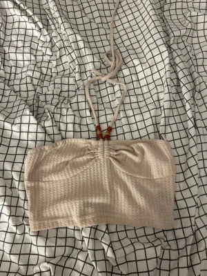 Beige halterneck topp från SHEIN - Säljer en beige halterneck topp från SHEIN i storlek S. Toppen har en ribbad struktur, knytband i nacken med träpärlor och är axelbandslös. Perfekt till sommaren och enkel att matcha med olika stilar.