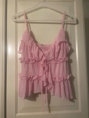 Söt rosa volangtopp💓 - Säljer denna supersöta Zara liknande rosa linnetoppen med tunna axelband, volanger och knyt framtill i storlek XS💓Perfekt till sommaren och passar till både jeans och kjol. Toppen har lite spruckna sömmar vid ena framkanten (se bild) men det är inget som påverkar kvaliteten💓Hör av er vid frågor!!