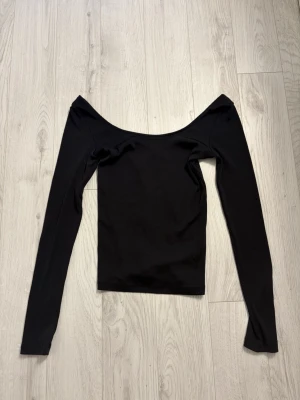 Svart offshoulder topp från H&M - Säljer en svart offshoulder topp från H&M i ribbad bomull. Toppen har lång ärm och en snygg croppad passform som sitter tight. Perfekt att styla med höga jeans eller kjol för en trendig look.