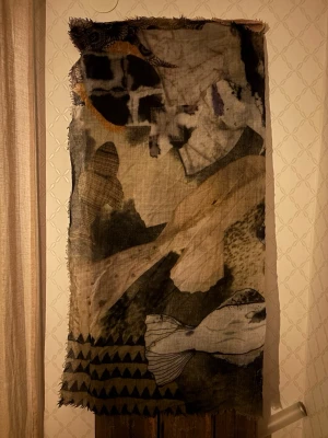 Mönstrad ullsjal från Beck Söndergaard - Unik sjal i 100% ull från Beck Söndergaard med konstnärligt fiskmönster i beige, svart, grått och röda detaljer. Sjalen har råa kanter och ett bohemiskt uttryck med handritad känsla och olika grafiska inslag. Perfekt för dig som vill sticka ut med en kreativ och cool look.