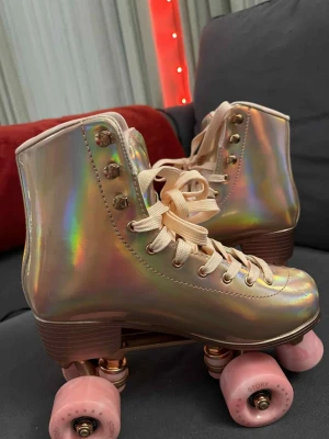 Story Glacier Shiny Gold rullskridskor 39 - Säljer ett par riktigt snygga rullskridskor från Story, modell Glacier Shiny Gold. Skorna har ett holografiskt guldigt yttre, ljusrosa snörning och matchande rosa hjul. Perfekt för dig som vill sticka ut på rinken eller gatan! Klassisk retrostil med högt skaft.
