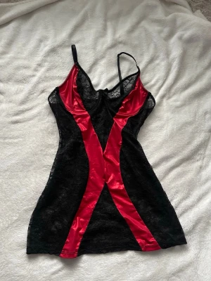 Svart och röd spetsnattlinne med satin - Supersnyggt nattlinne i svart spets och röd fakeläder. Vet tyvärr inte storlek eller märke då lappen har klippts av, men lite större kupa, typ runt B-C. Går att ändra banden i storleken, går precis precis till under rumpan!