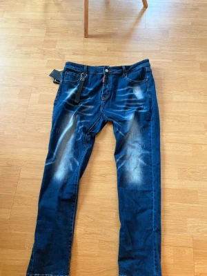 Dsquared2 New Rider Jeans – Made in Italy - Säljer ett par Dsquared2 New Rider jeans i mörkblå tvätt med slitningar och ljusa detaljer. Klassisk femficksmodell med tightare benslut och snygg Dsquared2-patch bak. Tillverkade i Italien i mjukt jeansmaterial. Perfekta för dig som gillar streetwear och premiumkänsla.