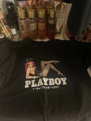 Svart Playboy t-shirt  - Svart t-shirt från Playboy med stort anime-inspirerat tryck framtill. Motivet visar en tecknad tjej i klassisk bunny-outfit och texten 'PLAYBOY' i vitt. 