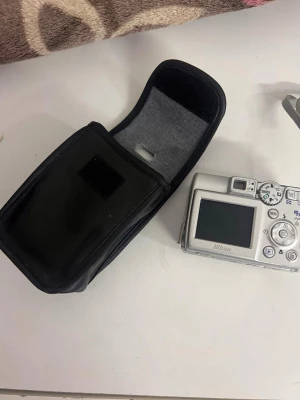 Nikon Coolpix 5600 - Nikon Coolpix 5600 digitalkamera med 5.1 megapixlar, 3x optisk zoom och röda-ögon-reducering. Kameran säljs med originalväska. Viss kosmetisk slitage syns, batteriluckan är öppen på bilderna men verkar hel.