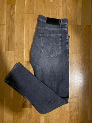 Mörkgrå washed jeans från Tiger of Sweden - Snygga mörkgrå jeans från Tiger of Sweden med klassisk femficksdesign och diskreta slitningar framtill. Jeansen har slim passform och raka ben, tillverkade i mjukt jeanstyg med lite stretch för extra komfort. Perfekta för en stilren look.