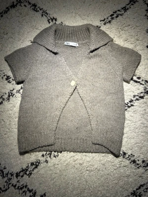 Beige stickad kofta från Zara - Säljer denna populära kortärmade stickade koftan från Zara, med bred krage och en dekorativ knapp framtill. Jag är öppen för prisförslag, du kan även köpa fler saker av mig för att få ett bättre pris!🥰