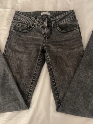 Perfekta lågmidjade svarta/gråa jeans från Gina Tricot - Snygga svarta jeans från Gina Tricot i modellen Perfect Jeans. De har en tvättad look, raka ben och klassiska fickor med lock och knapp bak. Jeansen har normal passform och är tillverkade i jeansmaterial med tydliga sömmar.